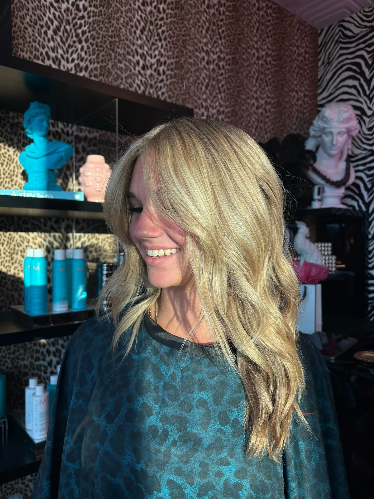 A smiling client with long blonde highlighted waves styled by Kyrin